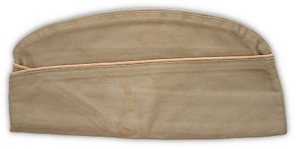 Left side view of the khaki cotton field cap. The cap had a bellows crown and a turned‐up curtain that crossed in the front. Authorization was given for the cap to be trimmed in branch of service colored cord‐edge braid. The piping was worn in much the same manner that branch of service cords were worn around the crown of the olive‐drab service hat. In this case the buff‐colored trim indicates the Quartermaster Corps. Left side view of the khaki cotton field cap. The cap had a bellows crown and a turned‐up curtain that crossed in the front. Authorization was given for the cap to be trimmed in branch of service colored cord‐edge braid. The piping was worn in much the same manner that branch of service cords were worn around the crown of the olive‐drab service hat. In this case the buff‐colored trim indicates the Quartermaster Corps.