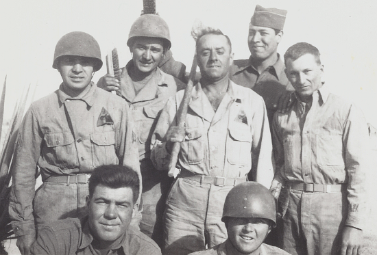 Men of the 11th Armored Division most likely in the California‐Arizona Maneuver Area in late 1943.   The first three men standing from the left wear two‐piece herringbone twill work uniforms with the jacket tucked inside the trousers.  Note the 11th Armored Division shoulder sleeve insignia is being worn above the left breast pocket and three of the men are wearing the M‐1 helmet liner for their headgear.