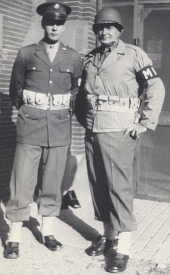 Two soldiers stand side b side; on the left the wool sevice uniform is worn with leggings for field wear, and on the right the new olive drab field jacket is worn with steel helmet