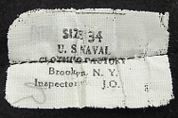 Pictured is the label containing the size and contract number for the dress blue jumper. It was located on the right, rear of the jumper and attached at the hem line. This label also provided a space for an inspector's mark.  The label was removed prior to wearing and is therefore seldom seen.  If the jumper was manufactured by an outside contractor and not the Naval Clothing Factory, the label had a contract number printed on the reverse side.