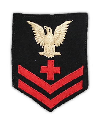 Petty Officers 1st, 2nd, and 3rd class wore a rating badge on their jumpers between the shoulder and elbow.  When worn on the dress blue jumper, rating badges consisted of a white eagle, white specialty mark, and red chevrons on a blue background. Men of the Seaman Branch wore the rating on the right arm and all other branches wore the rating on the left arm.  Badges were manufactured so that the eagle would face forward according to which sleeve it was to be placed.  Pictured here is a close-up of the badge on the arm of the jumper shown below and is that of a Second Class Pharmacist's Mate. In this specific exception, the specialty mark of the cross is done in red instead of white.