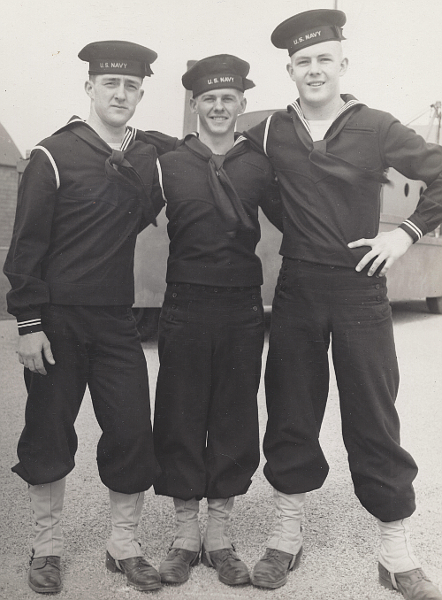 Three sailors pose for a photo at the Great Lakes Naval Training Station in 1945.  They wear the Dress Blue A uniform with high-top shoes and leggings.  Their jumpers have two white cuff stripes indicating they are Second Class Seamen and on the right shoulder they wear the white braid of the Seaman Branch.  All are wearing the shortened 1944 style jumper.  The wide hemline, a telltale sign of the 1944 model jumper, is clearly visible on the waist of the man on the left.