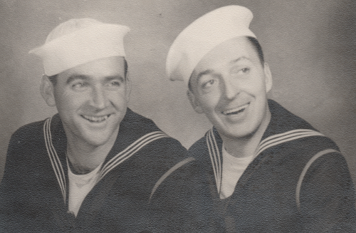 Clifford Harrior (left) and Charlie Harmen (right) wear the Dress Blue B uniform featuring the white hat.  Here, the red braid on the left shoulder is prominently displayed indicating both men are members of the Artificer Branch (Engine Room Force).