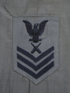 First class petty officer's gray rating badge with gunner's mate specialty mark.